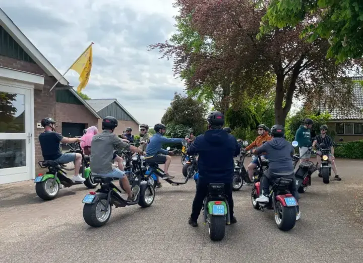 Groep collega's met helmen op e-choppers verzamelt zich bij een boerderij in Twente voor de start van een bedrijfsuitje