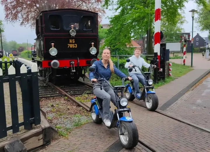 Twee collega's rijden op e-choppers langs een historische stoomtrein tijdens een personeelsuitje nabij Hengelo